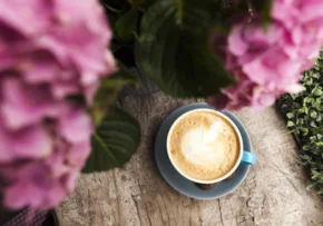 top-view-pink-flower-tasty-coffee-with-frothy-foam-wooden-surface | Foto: freepik.com